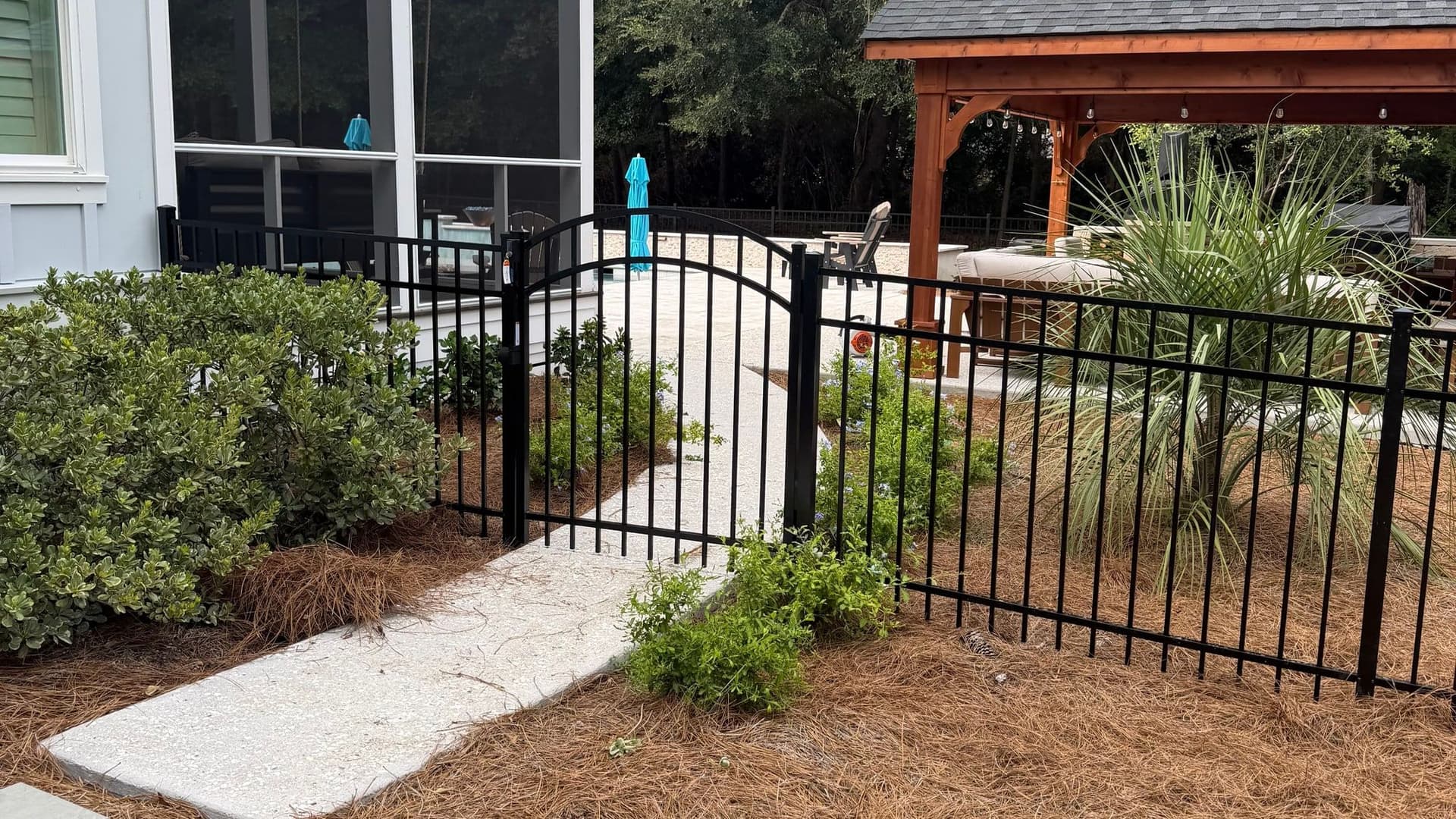 Ornamental aluminum fence and gate installed by Walter Handyman LLC beside a Charleston backyard patio